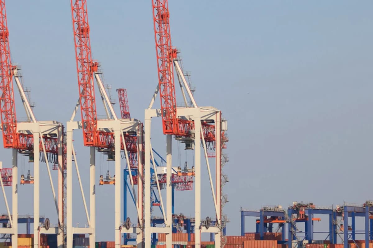 Illustrative photograph: Red and white terminal cranes above rows of containers.