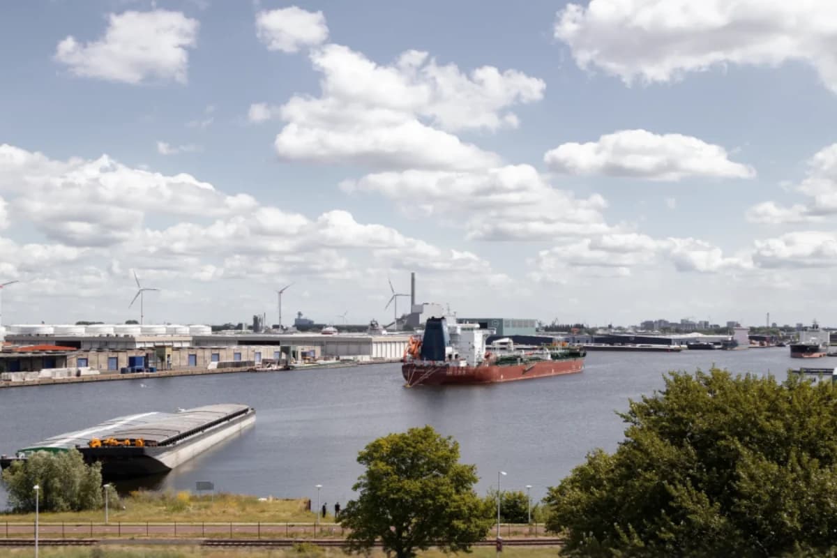 A ship in a port channel, quayside buildings and clouds over the water.